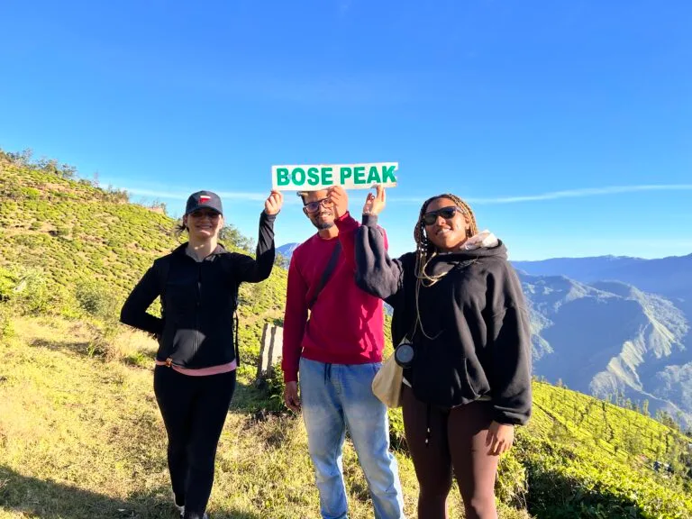 Three retreat guests smiling beside a Rose Peak sign on a mountain top