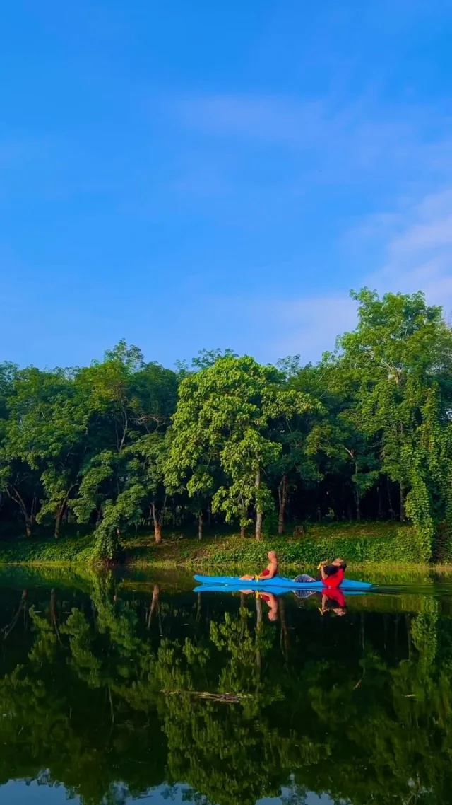 A kayaker crossing a green lake ringed by forest
