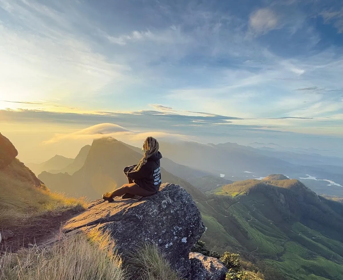 A person meditates on a rock outcrop as the sun rises over a valley of clouds
